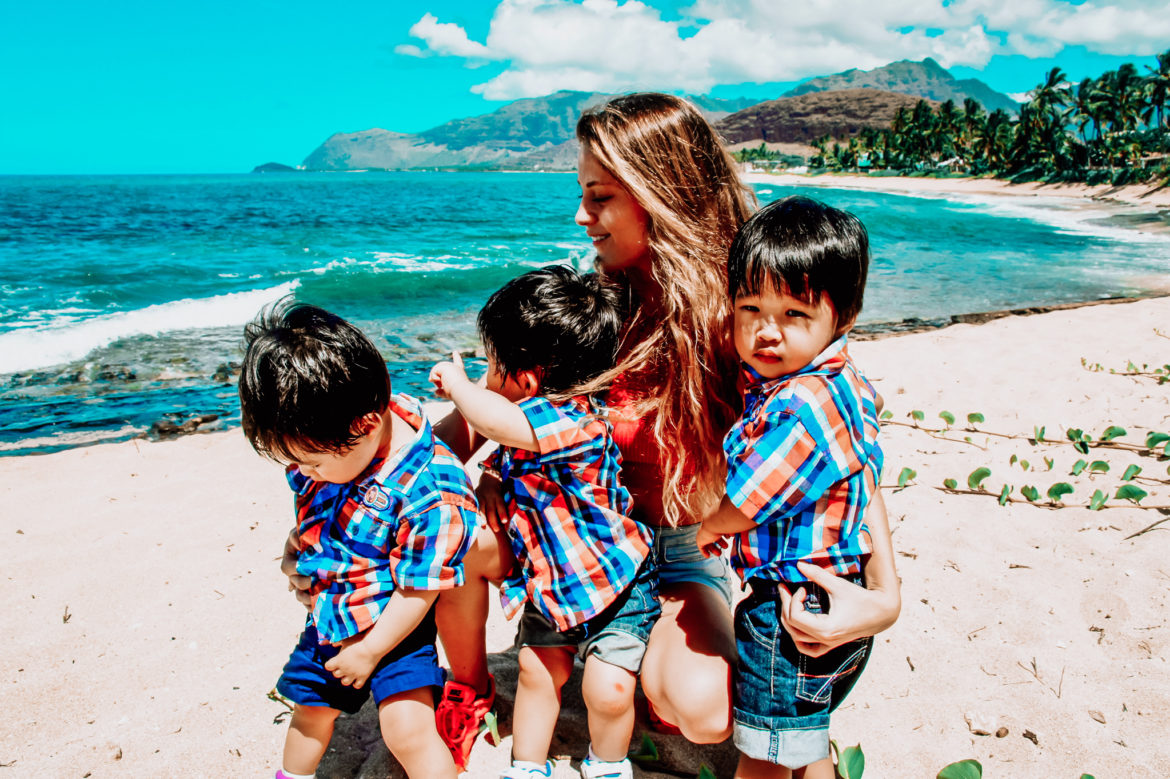 Au pair providing child care to set of multiple children — triplets on the beach.