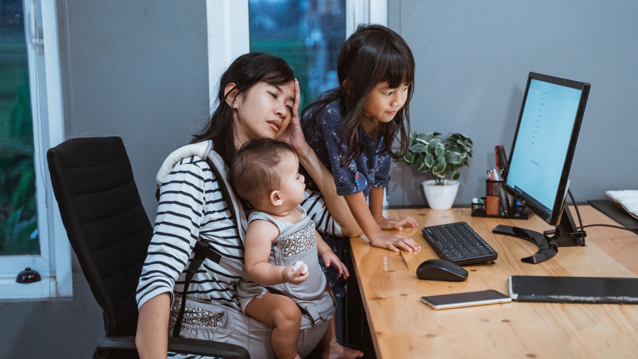 Stressed parent with two children sitting at computer desk