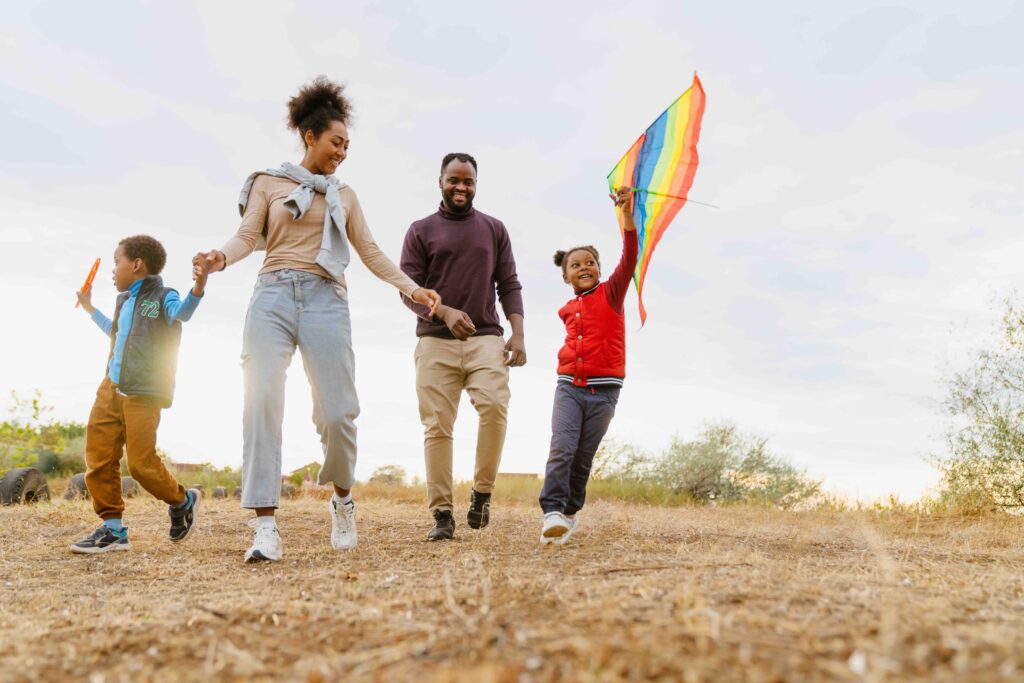 family laughing and flying kite while running together outdoors