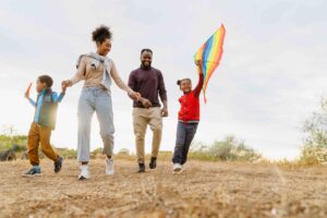 family laughing and flying kite while running together outdoors