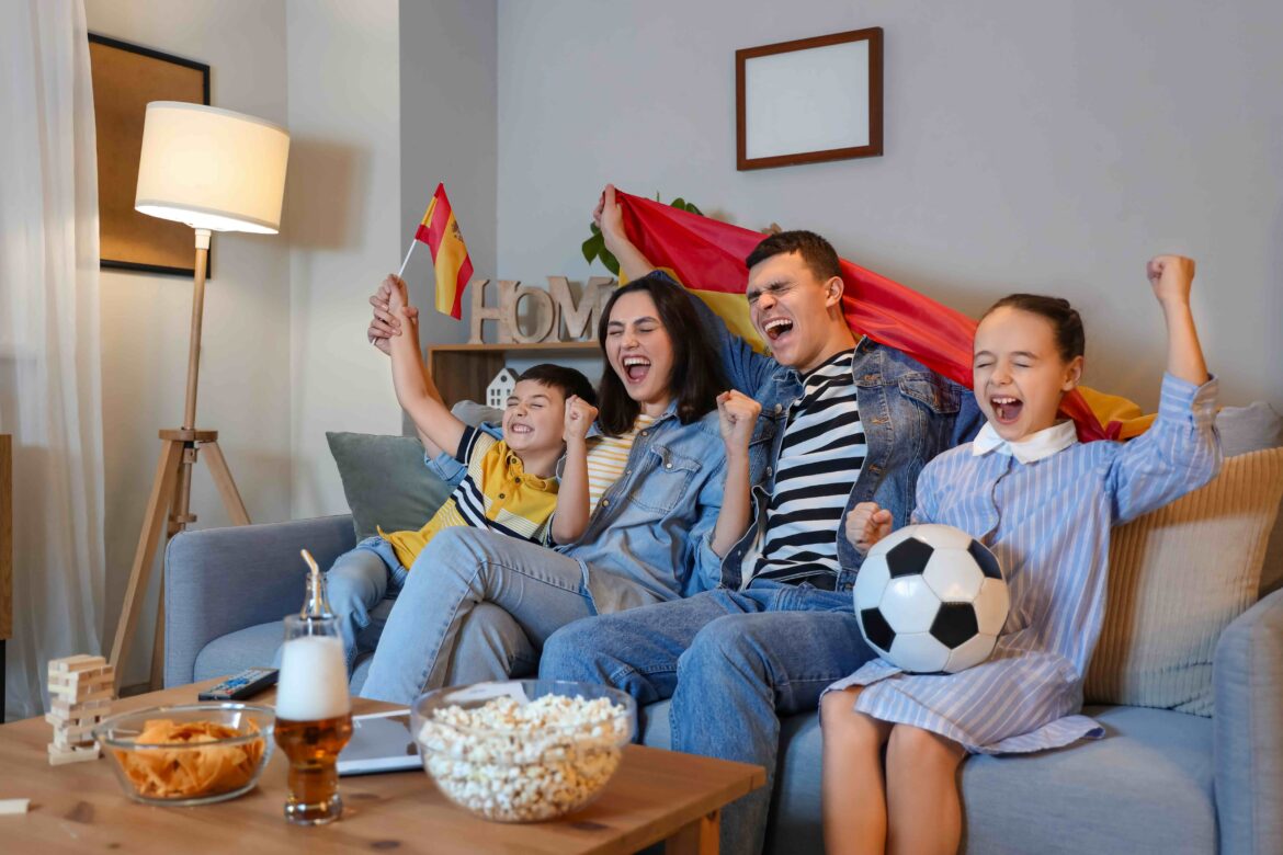 family watching soccer game at home holding flag of spain